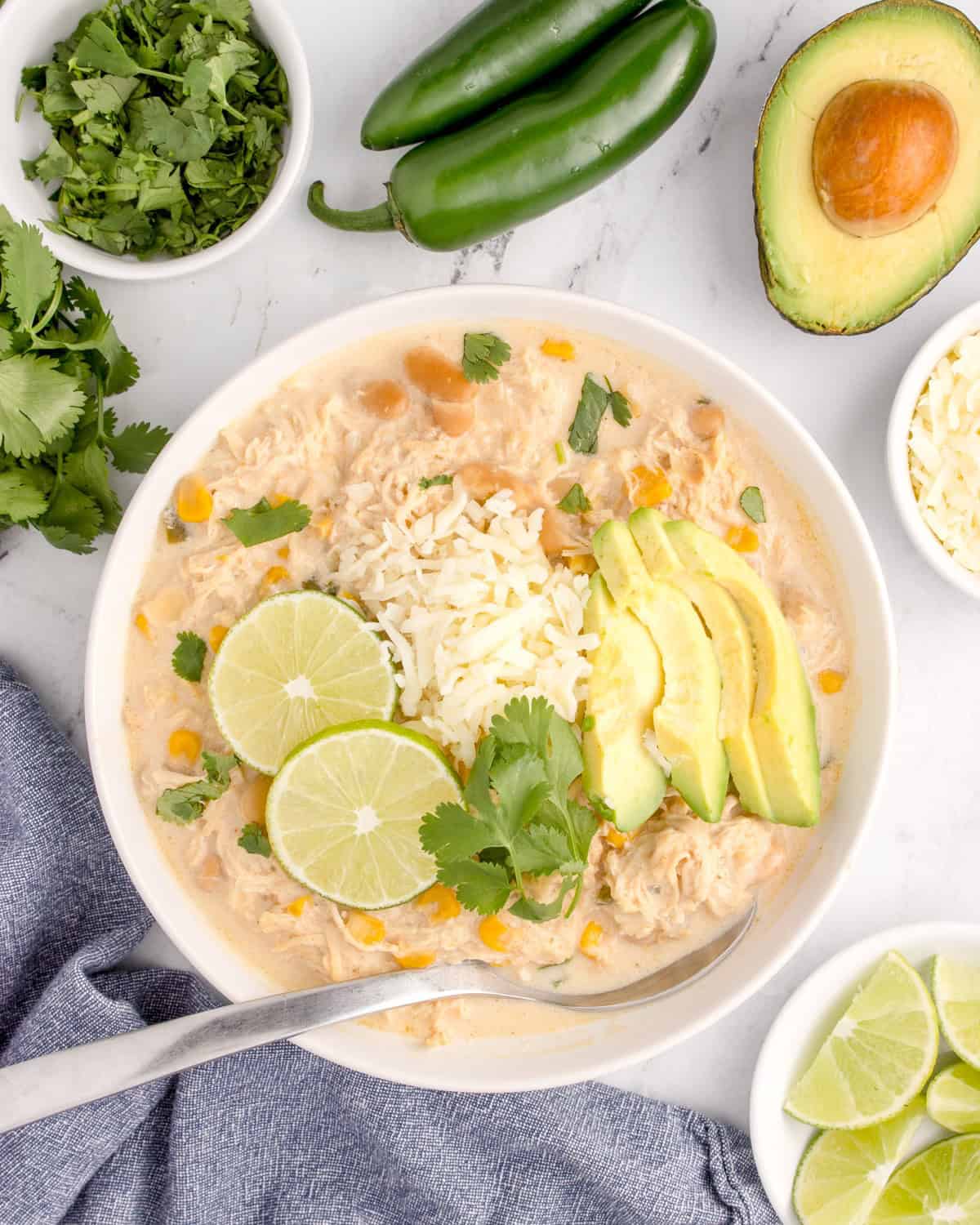 white chili chicken topped with cilantro, avocado, cheese, and lime wedges